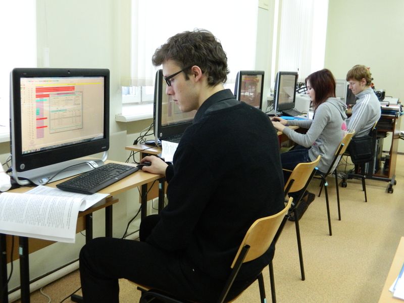 Цветное фото. В компьютерном классе вдоль стены стоят компьютеры, на которых находятся компьютеры, за ними сидят 3 студента, выполняющие учебные задания.
